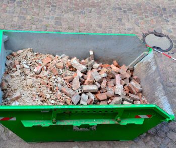 Caçamba com entulho de construção civil contendo tijolos e concreto, pronta para coleta de resíduos da obra.