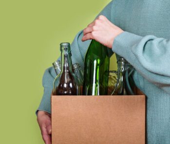 Pessoa segurando caixa com garrafas de vidro para reaproveitamento e reciclagem de resíduos sólidos.