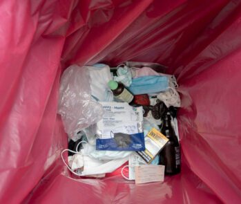 Resíduos hospitalares descartados em saco vermelho, incluindo máscaras, medicamentos e embalagens, ilustrando a importância da classificação correta segundo a legislação sanitária.