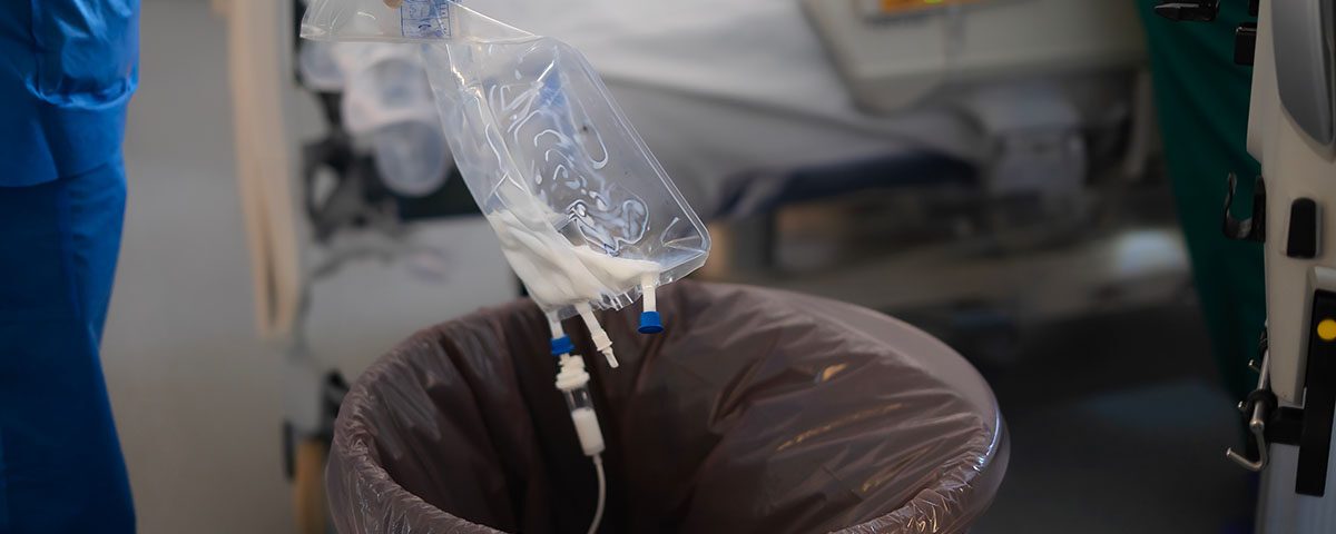 Profissional de saúde descartando bolsa de soro usada em recipiente adequado para resíduos hospitalares em ambiente clínico.