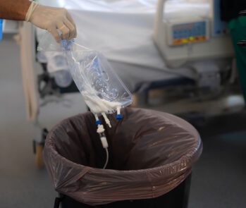 Profissional de saúde descartando bolsa de soro usada em recipiente adequado para resíduos hospitalares em ambiente clínico.