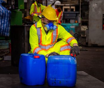Profissional com equipamento de proteção manuseando tambores de resíduos químicos, exemplificando quais são os resíduos perigosos e como fazer a gestão adequada.