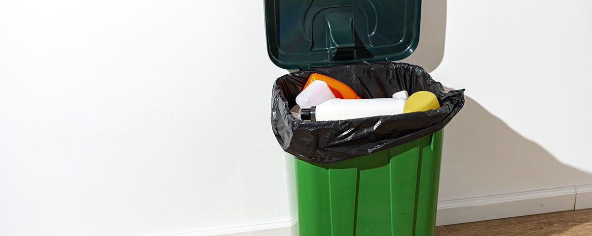 Lixeira verde com saco plástico preto contendo resíduos recicláveis, como embalagens plásticas, representando a separação correta de resíduos sólidos urbanos.