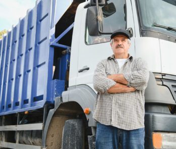 Motorista de caminhão de transporte de resíduos posa ao lado do veículo, ilustrando a importância do curso MOPP na gestão de resíduos.