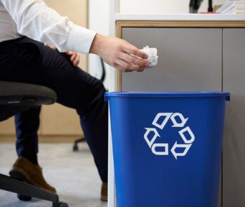 Profissional descartando papel em lixeira azul de reciclagem no escritório, exemplificando como implantar um projeto de coleta seletiva eficiente nas empresas
