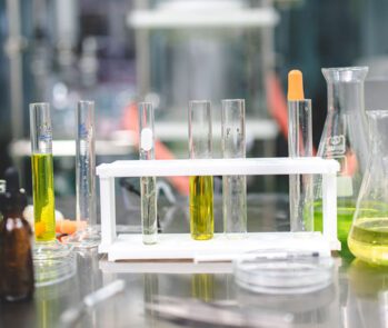 Materiais e reagentes químicos dispostos em bancada de laboratório, representando a importância da elaboração da FISPQ, FDSR e ficha de emergência na gestão de produtos perigosos.