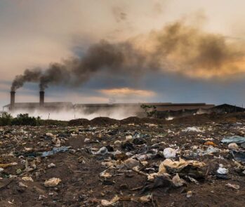 Imagem de incineradora industrial liberando fumaça preta, com acúmulo de resíduos sólidos em primeiro plano, ilustrando os impactos ambientais da incineração e a necessidade de critérios técnicos para o seu uso.