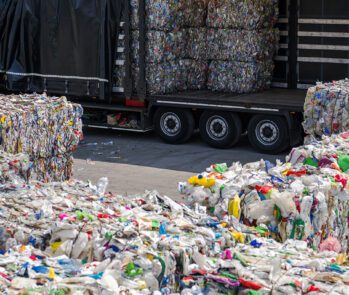 Grandes fardos de plástico prensado sendo carregados em um caminhão de grande porte em uma central de triagem ou reciclagem.