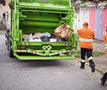Coleta de resíduos sólidos urbanos realizada por profissionais de limpeza pública com caminhão compactador em área residencial, conforme normas da gestão de resíduos sólidos.