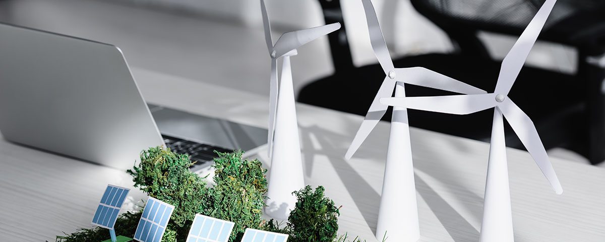 Maquete de energia renovável com turbinas eólicas, painéis solares e vegetação sobre mesa de escritório, representando sustentabilidade corporativa e certificação de destinação final de resíduos.