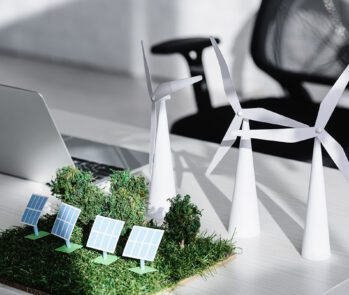 Maquete de energia renovável com turbinas eólicas, painéis solares e vegetação sobre mesa de escritório, representando sustentabilidade corporativa e certificação de destinação final de resíduos.