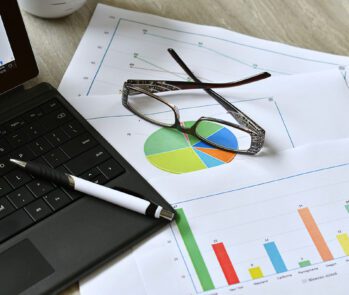 Planilha de gestão de resíduos com gráficos e relatórios sobre volume e tipos de descarte, ao lado de notebook e óculos sobre a mesa.
