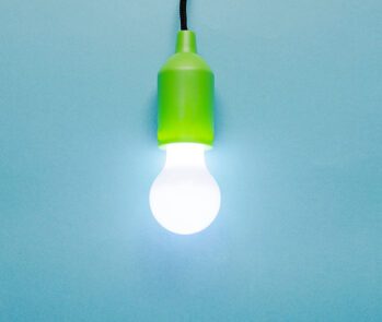 Lâmpada LED acesa com soquete verde em fundo azul, representando eficiência energética e descarte ambientalmente correto de resíduos eletrônicos.