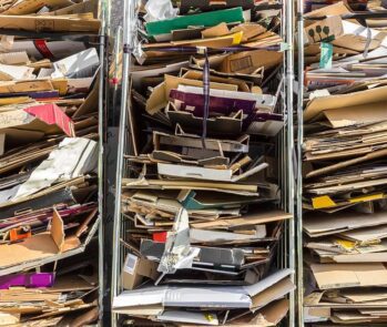 Pilhas de papelão prensado e organizado em estruturas metálicas, representando resíduos recicláveis prontos para coleta seletiva ou reciclagem.