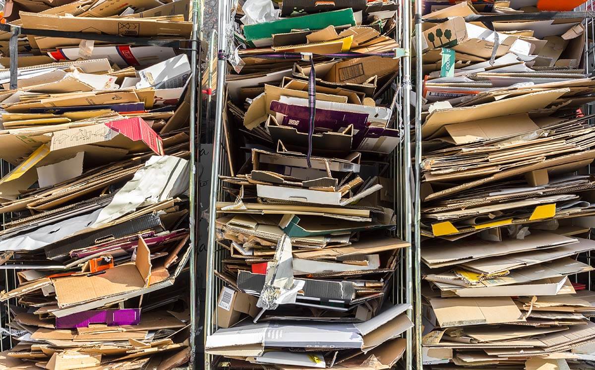 Pilhas de papelão prensado e organizado em estruturas metálicas, representando resíduos recicláveis prontos para coleta seletiva ou reciclagem.