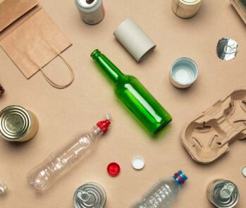 Itens recicláveis e reutilizáveis, incluindo vidro, plástico e metal, vistos de cima para ilustrar a separação de resíduos.