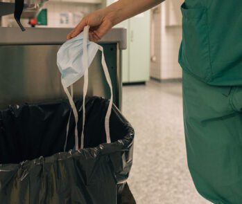 Profissional da saúde descartando máscara cirúrgica em lixeira hospitalar, ilustrando a importância do PGRSS e como elaborá-lo corretamente.