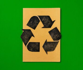 Símbolo de reciclagem preto estampado em caderno marrom sobre fundo verde — veja as principais perguntas e respostas sobre reciclagem.