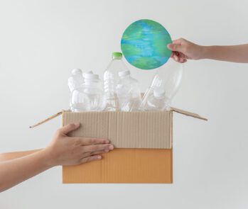 Mãos segurando caixa com garrafas plásticas recicláveis e planeta de papel, simbolizando sustentabilidade e gestão de resíduos com foco em impactos ambientais.